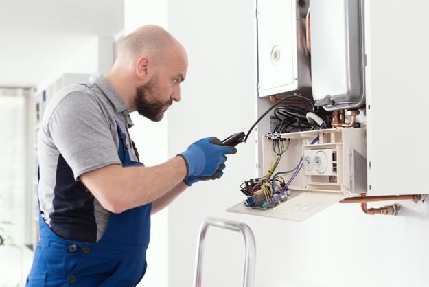 Mann in Arbeitskleidung arbeitet an einer Gastherme.