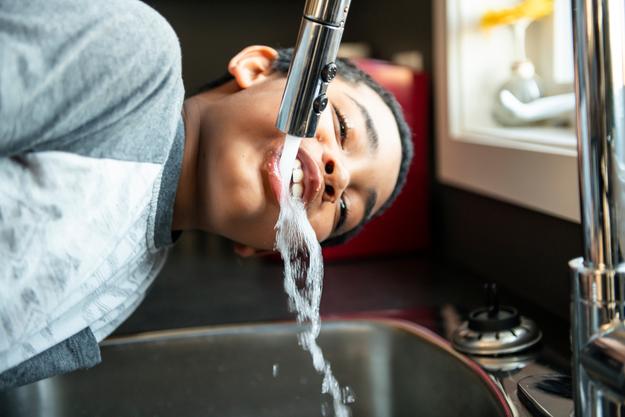 Kind trinkt Wasser, das direkt aus dem Wasserhahn fließt.